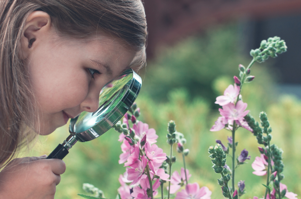 Image of little girl looking through a magnifying glass suggesting a return to curiosity after doing Safe & Sound Protocol