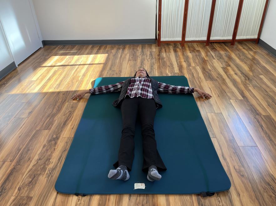 A student lying on the ground, with their arms out at 90-degree angles to their body