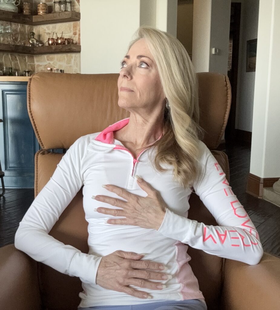 A seated woman placing one hand on her stomach and one hand on her heart