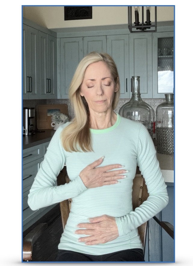 A woman standing, one hand on her heart and one hand on her abdomen